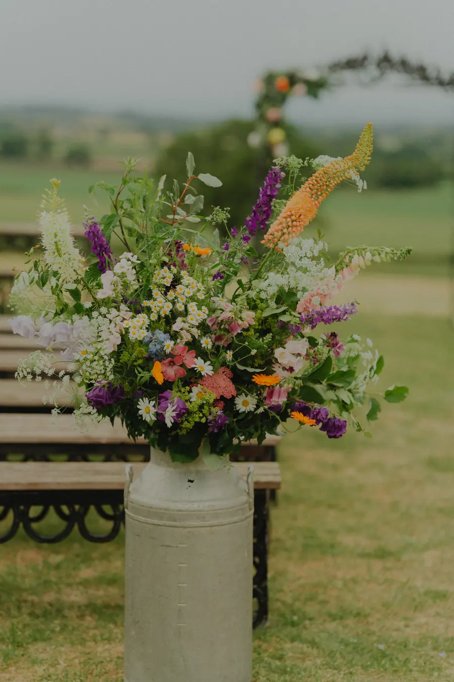Colourful flowers arranged in a milk churn beside the ceremony benches
