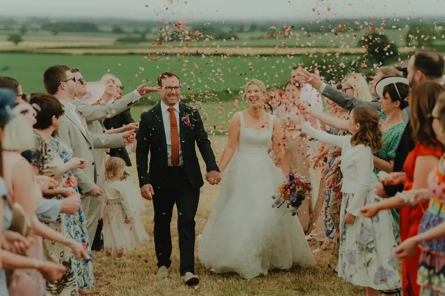 Guests throwing confetti as the couple walk from the outdoor ceremony