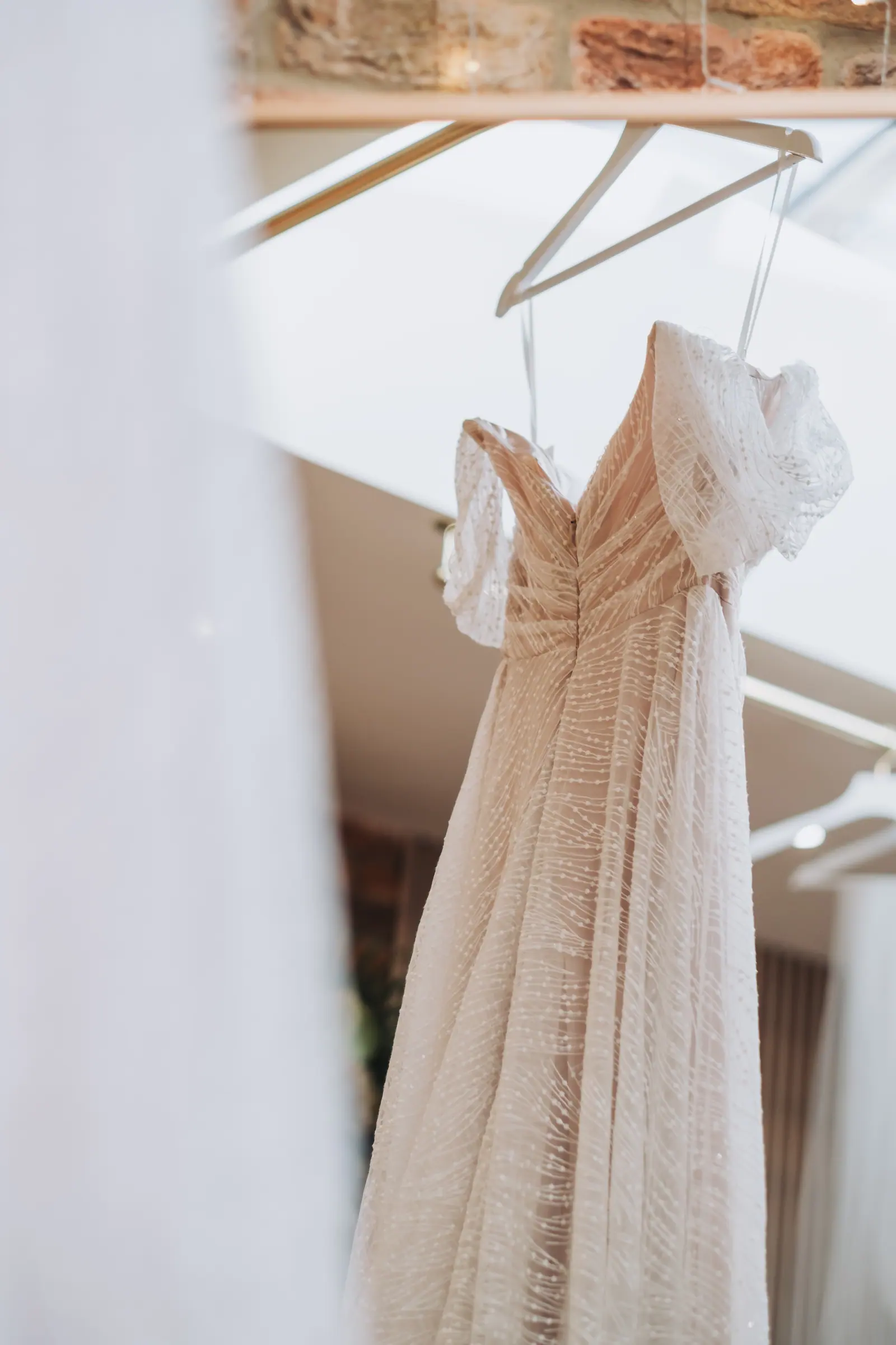 Evie-Mae's beaded wedding dress hanging against brick and pale walls
