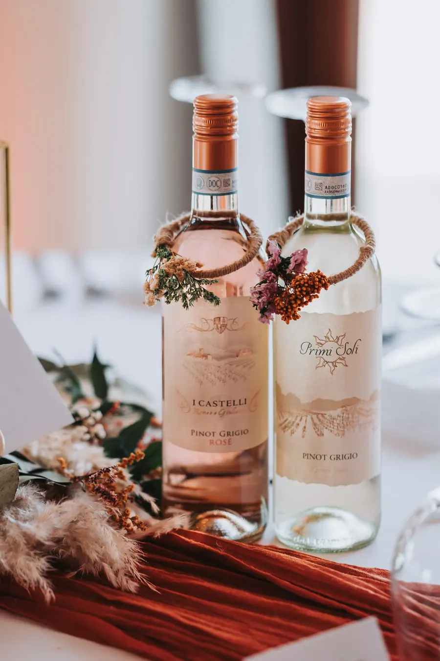 Two wine bottles decorated with small dried-flower wreaths on the table