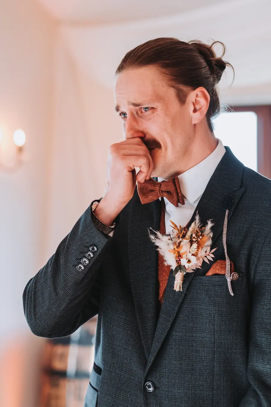 Joe covering his mouth while wearing a rust waistcoat and bow tie