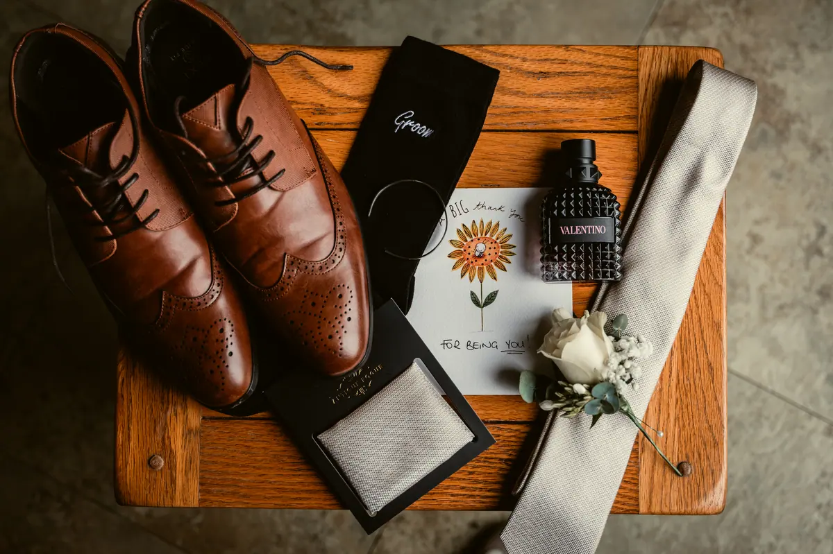 Brown shoes, dark tie, rings and white buttonhole arranged on wood