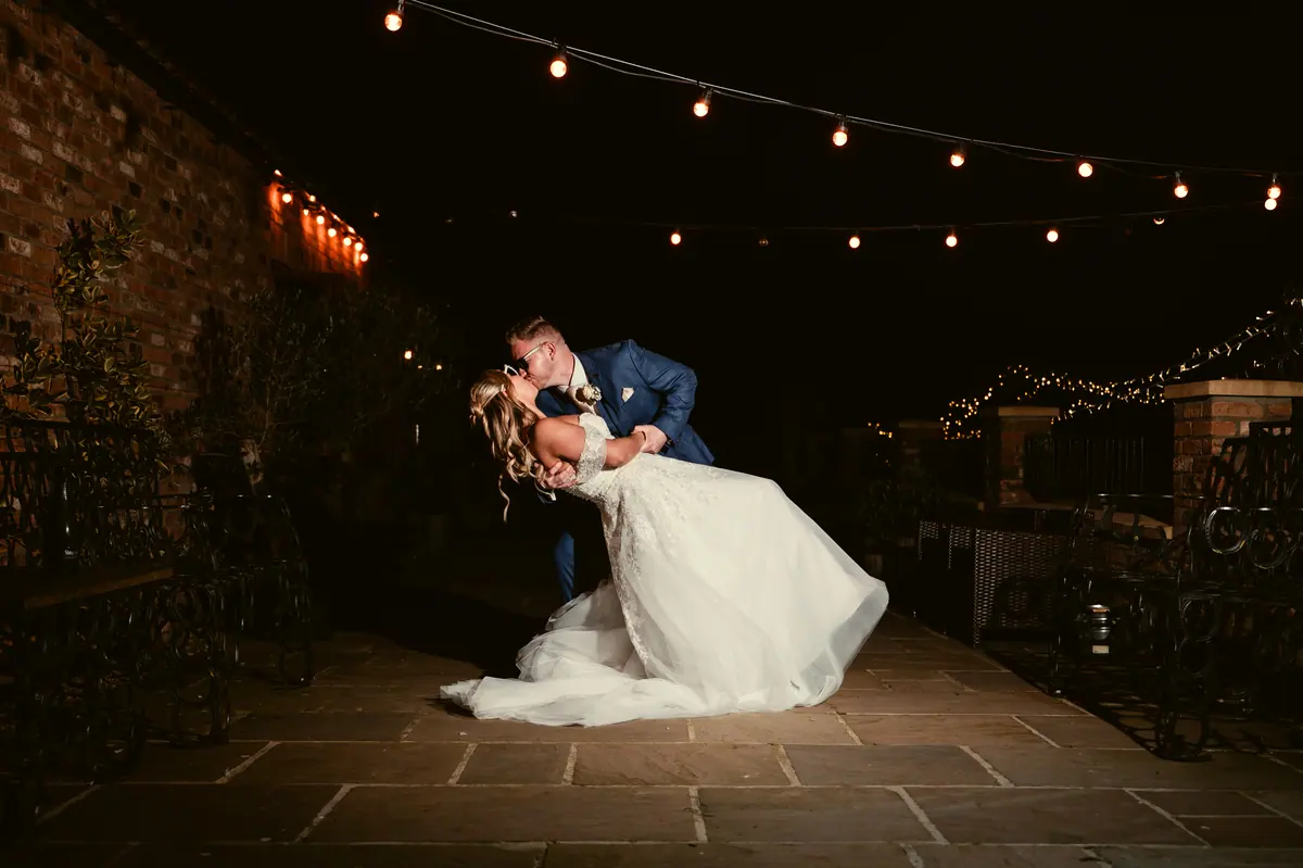 Jayrrd dipping Hayley beneath strings of courtyard lights after dark