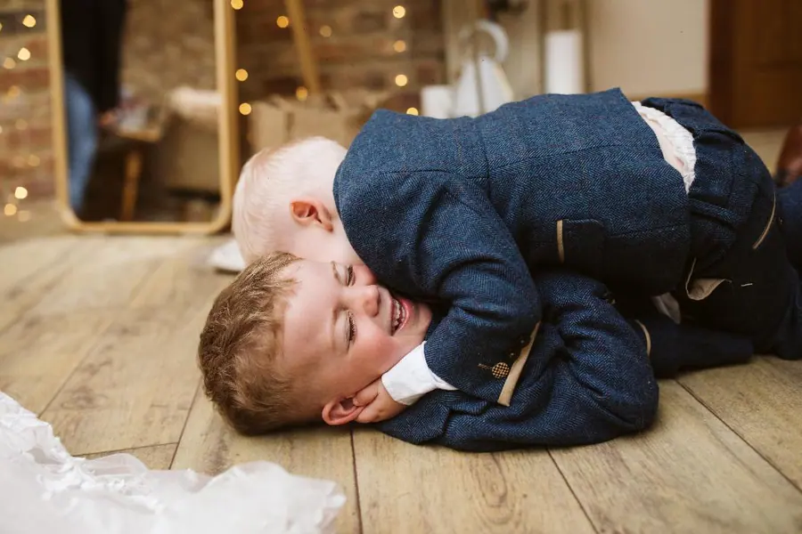Two young boys lying together on the wooden floor indoors
