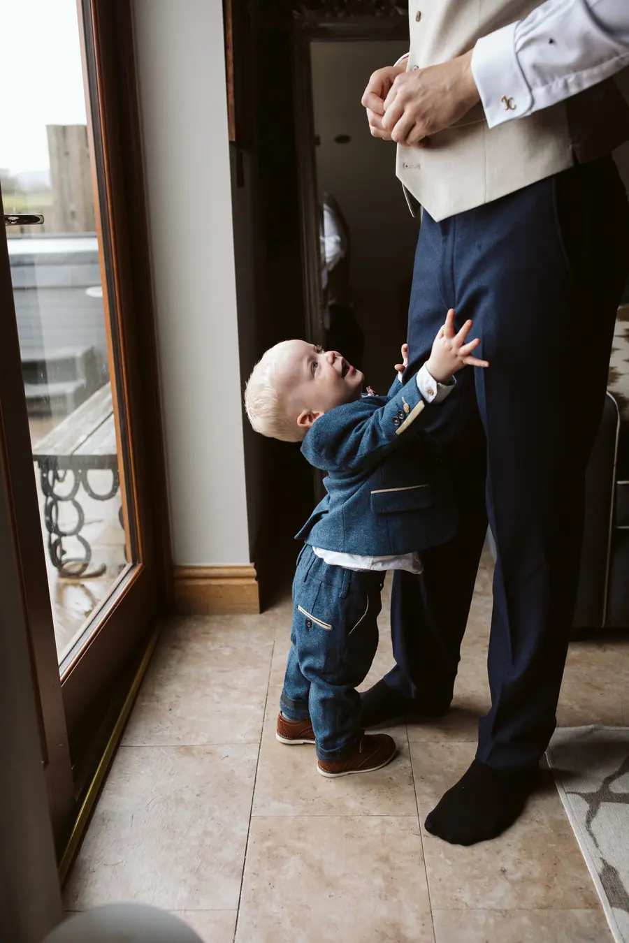 A young boy reaching up towards Jack beside a tall window