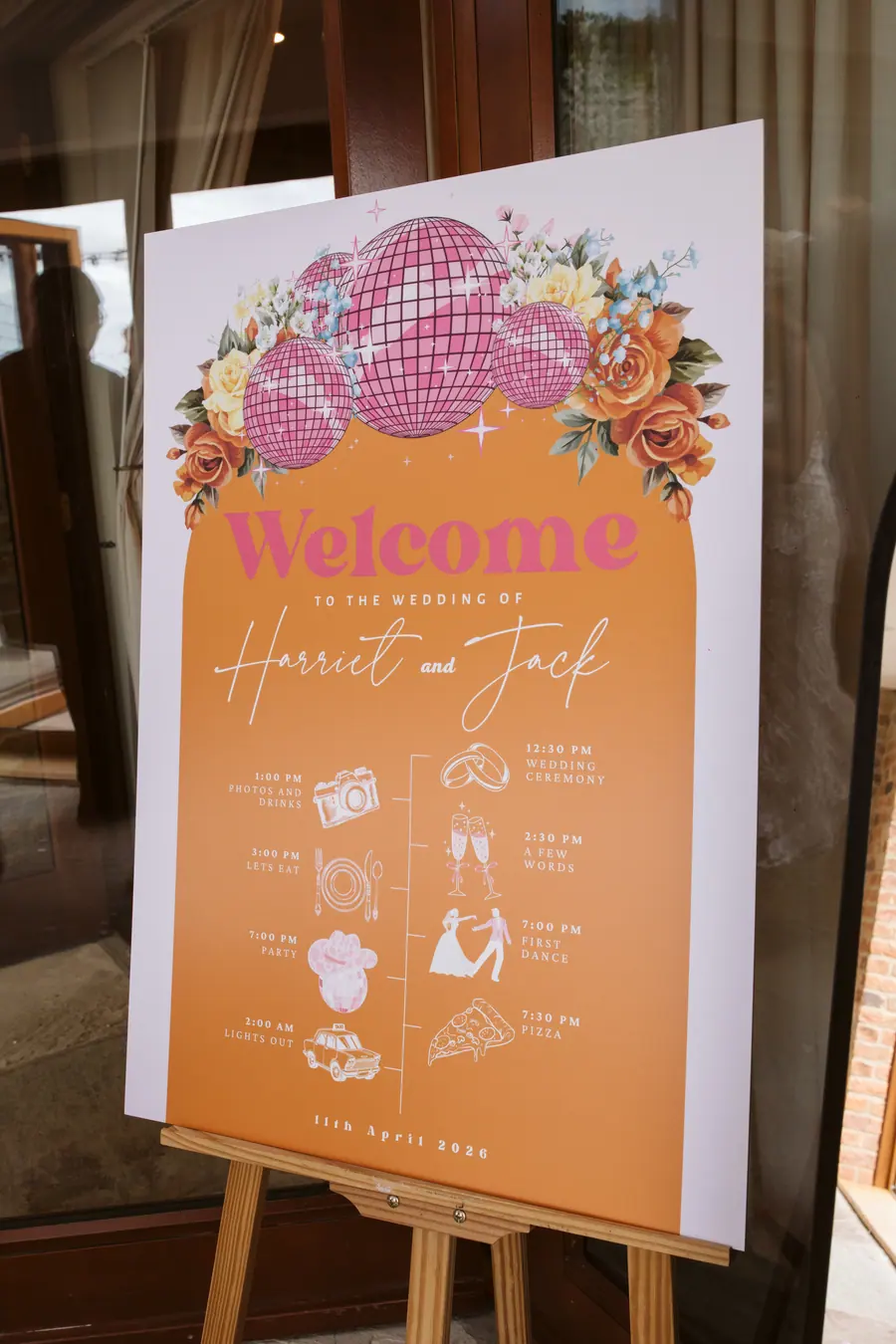 Orange welcome board decorated with flowers and illustrated wedding details