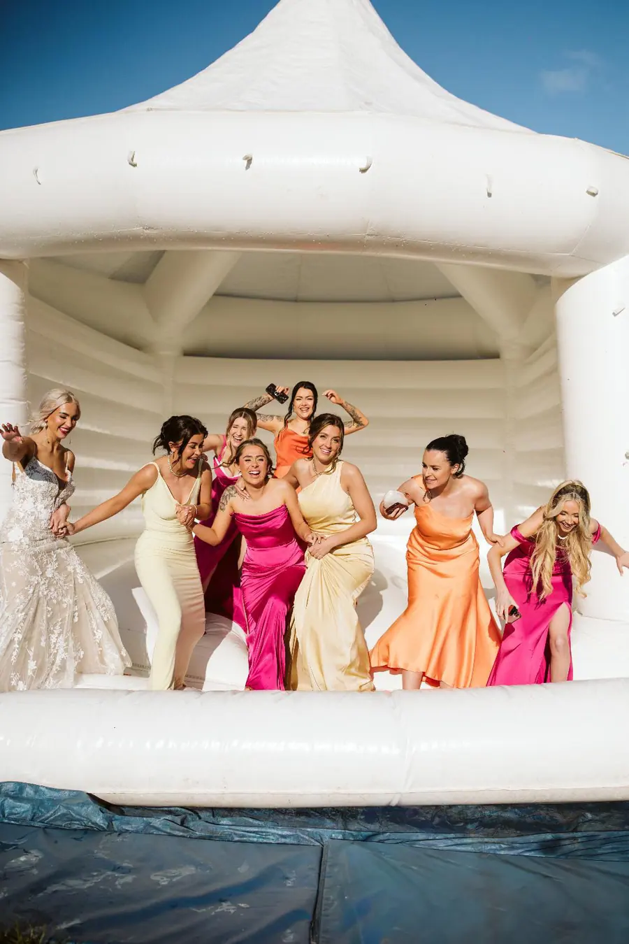 Wedding party in bright dresses gathered inside a white inflatable structure