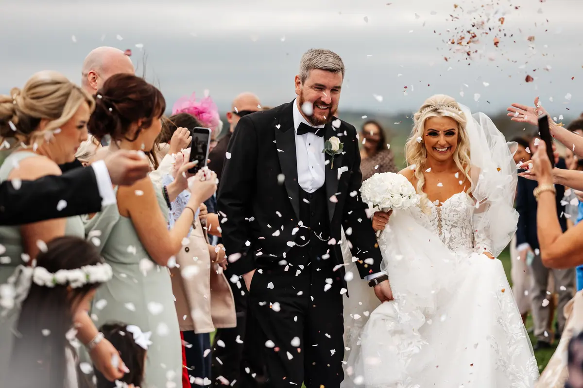 Guests throwing confetti around Jodie and Chris outside the brick barns