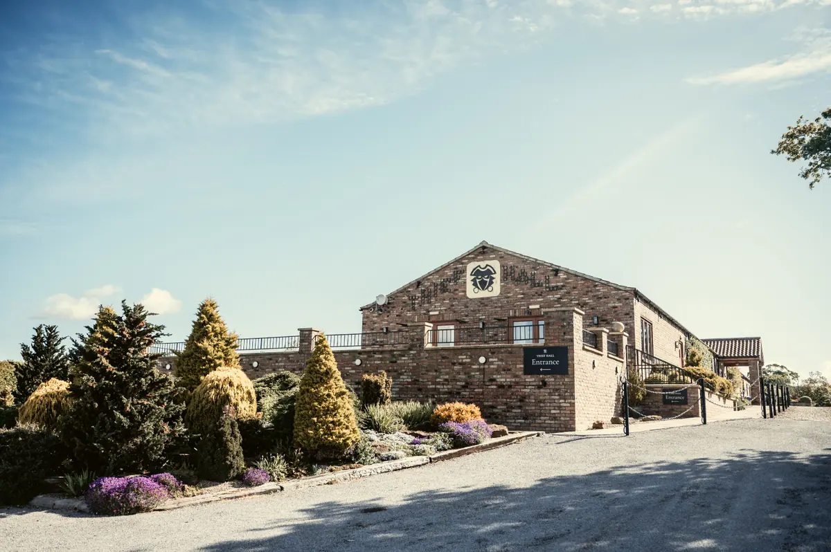Brick Thief Hall barns and planted entrance beneath a bright sky