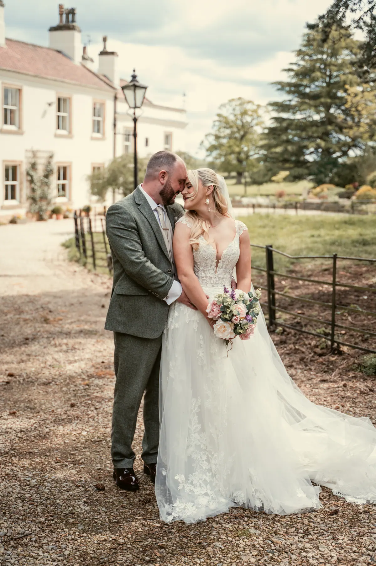 Katie and Chris standing beside a pale house and planted garden