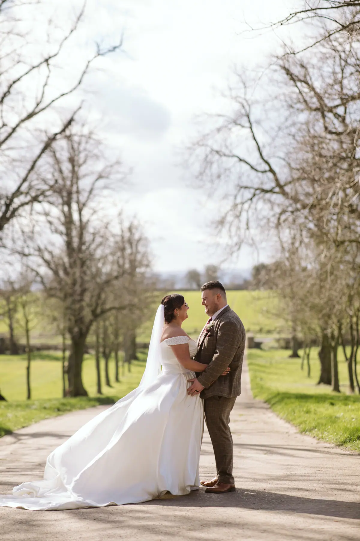 Katy and George kissing on the lane beneath bare spring trees