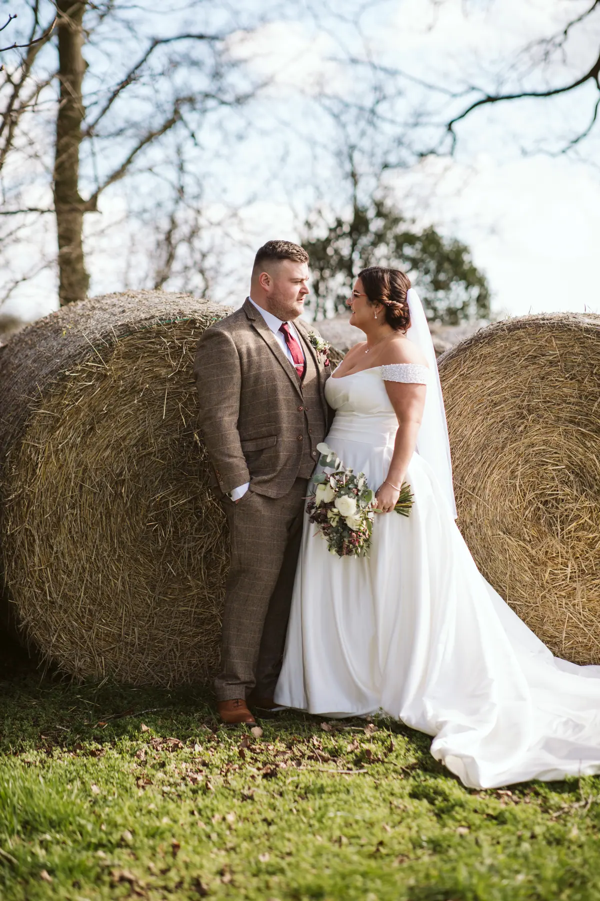 The couple standing beside round hay bales on green grass