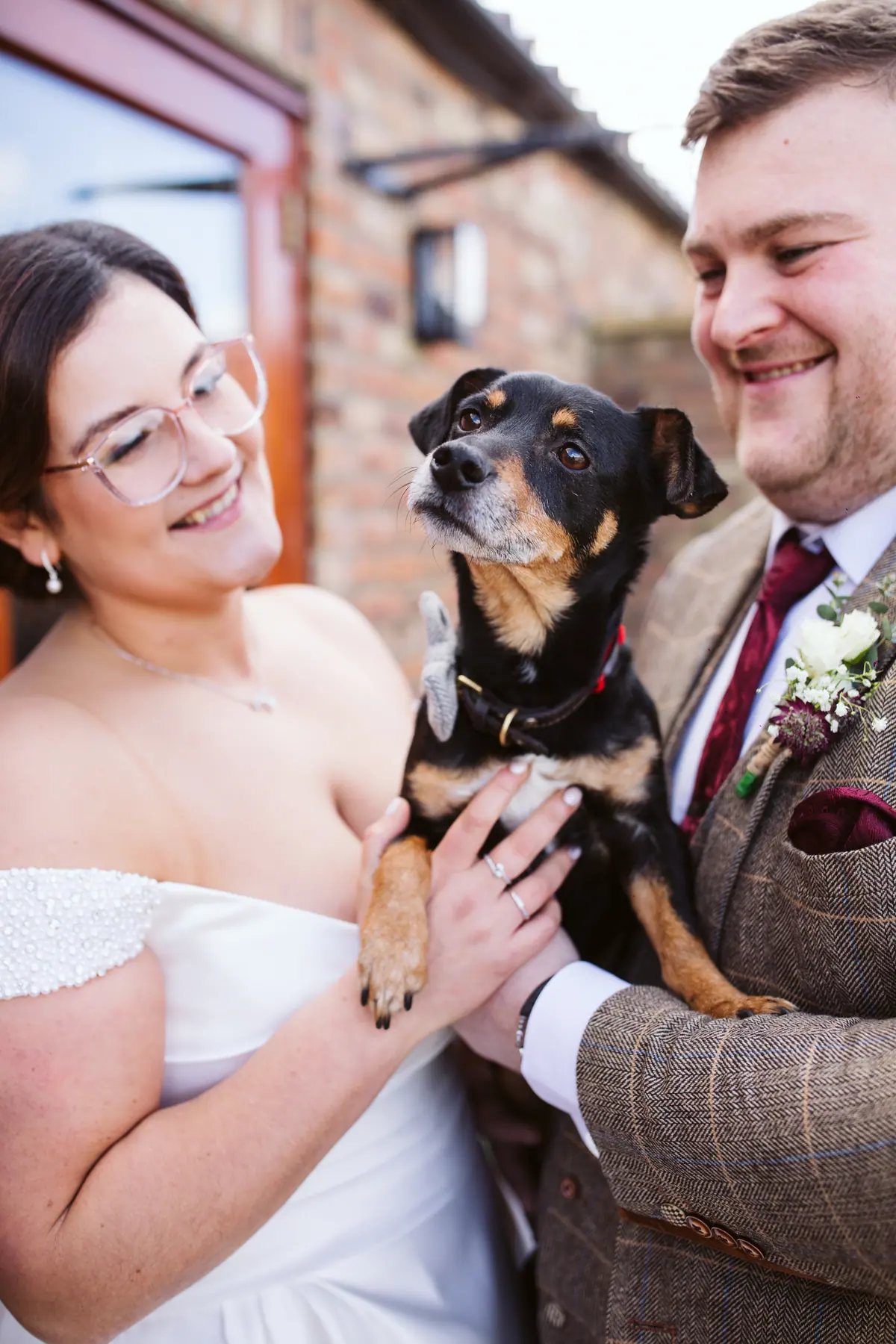 The couple holding a small black dog outside the brick barns