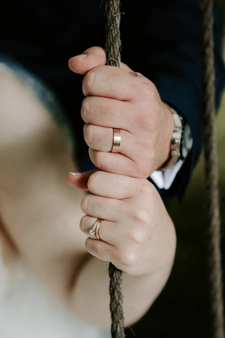Two ringed hands holding the rope of a woodland swing