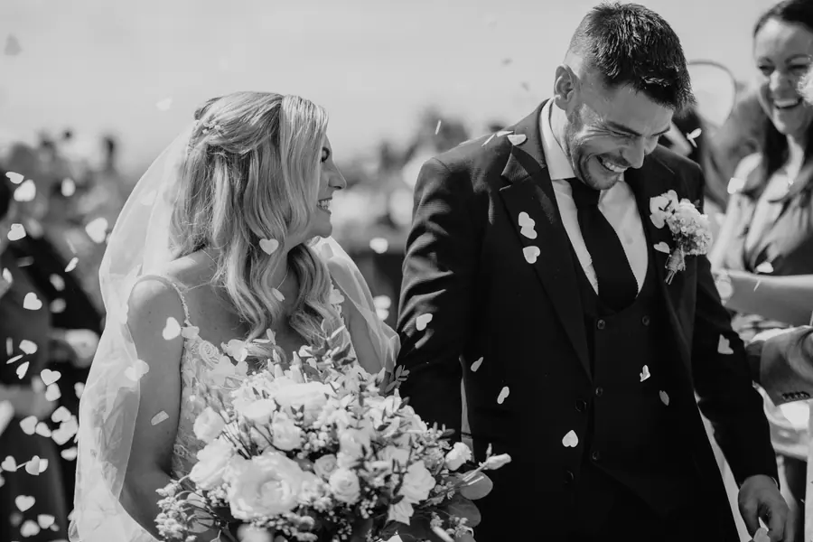 Confetti falling over Lauren and Iain as they walk between guests