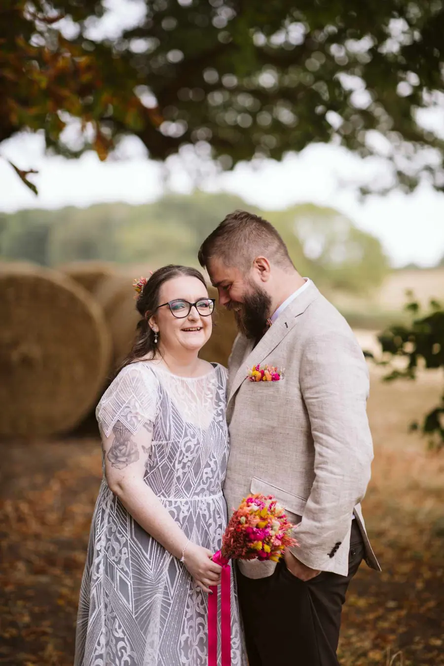 Lauren and Martin standing together beneath a tree beside the hay bales