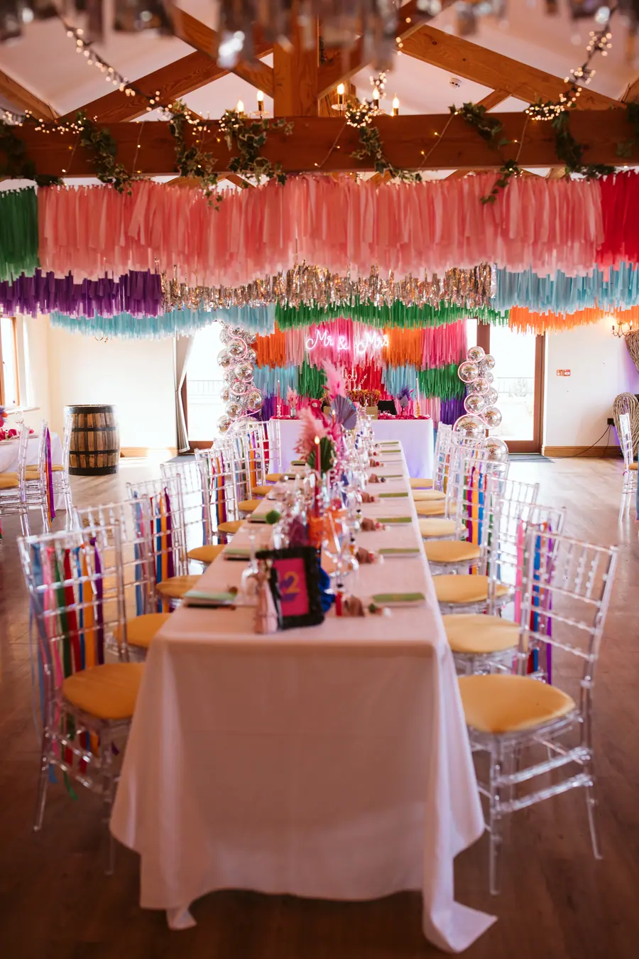 Long dinner tables beneath pink, purple, teal and silver hanging fringe