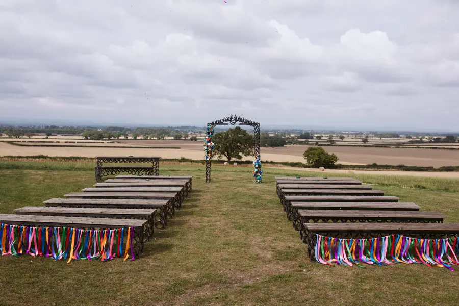 Outdoor ceremony benches decorated with coloured ribbons beneath a cloudy sky