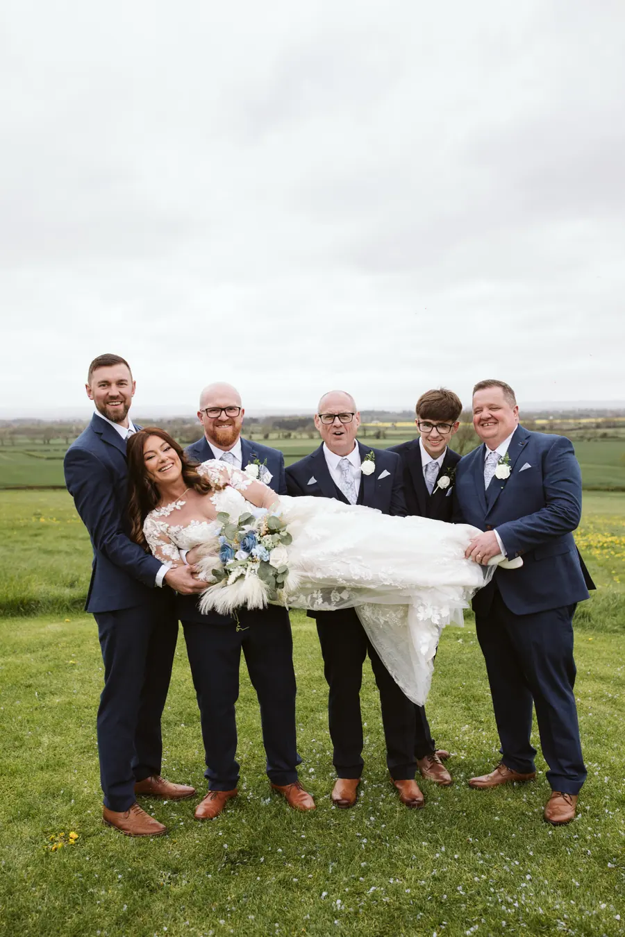 Five men holding Lisa horizontally against the open countryside fields