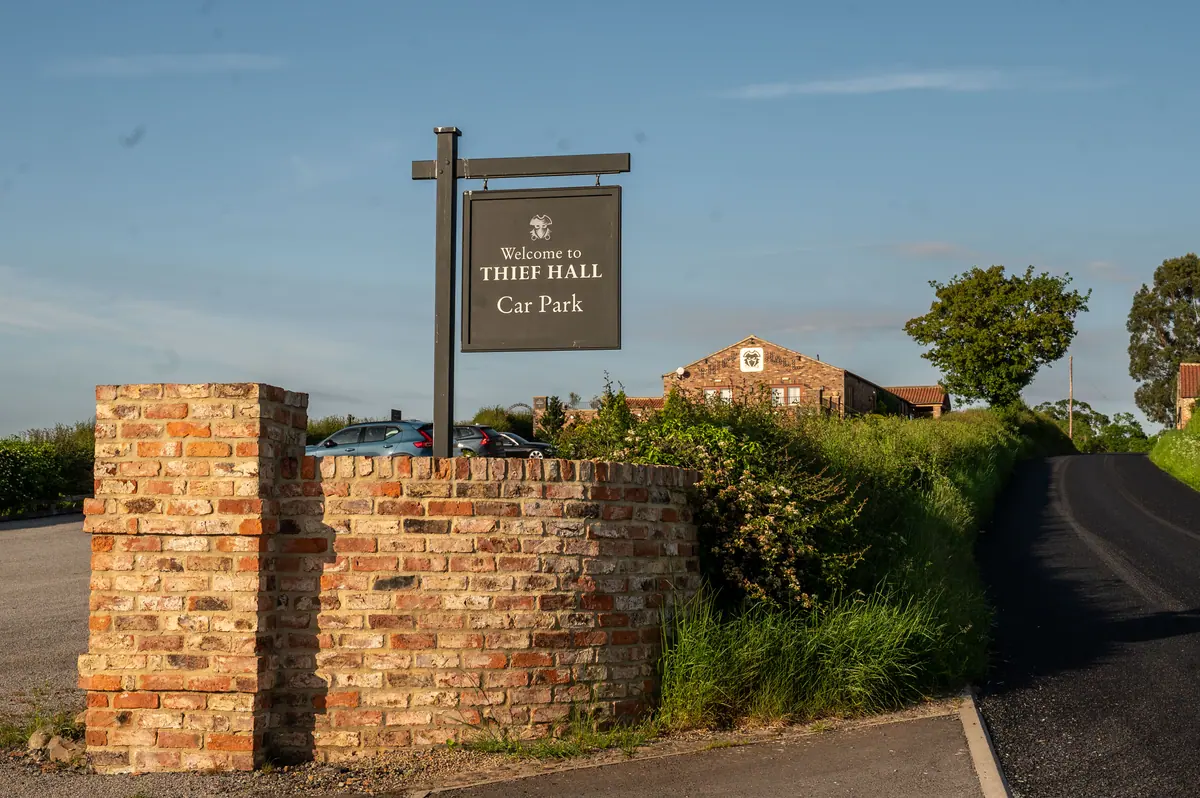 Thief Hall entrance sign above the lane with barns in view