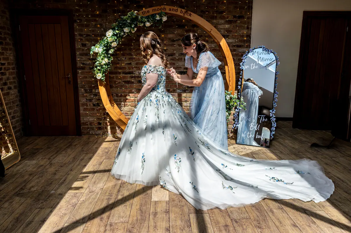 Megan standing in sunlight while a woman adjusts her floral gown