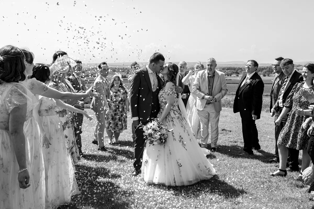Guests throwing confetti around Megan and Dan outside the brick barns