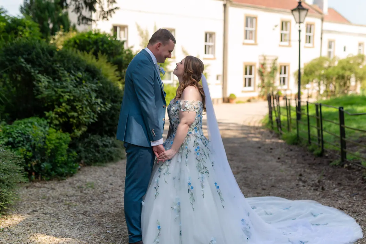 Megan and Dan touching foreheads beside the pale house and gate