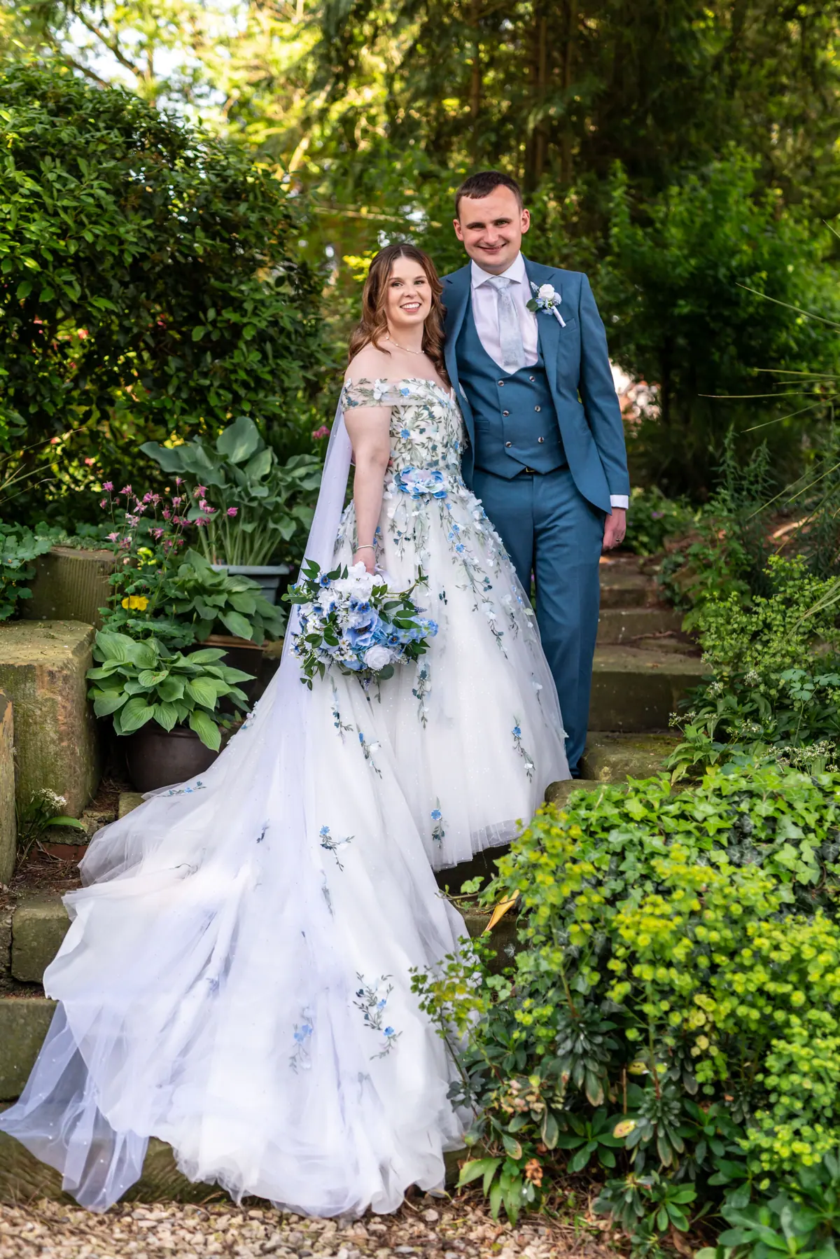 The couple standing together on a stone path surrounded by greenery