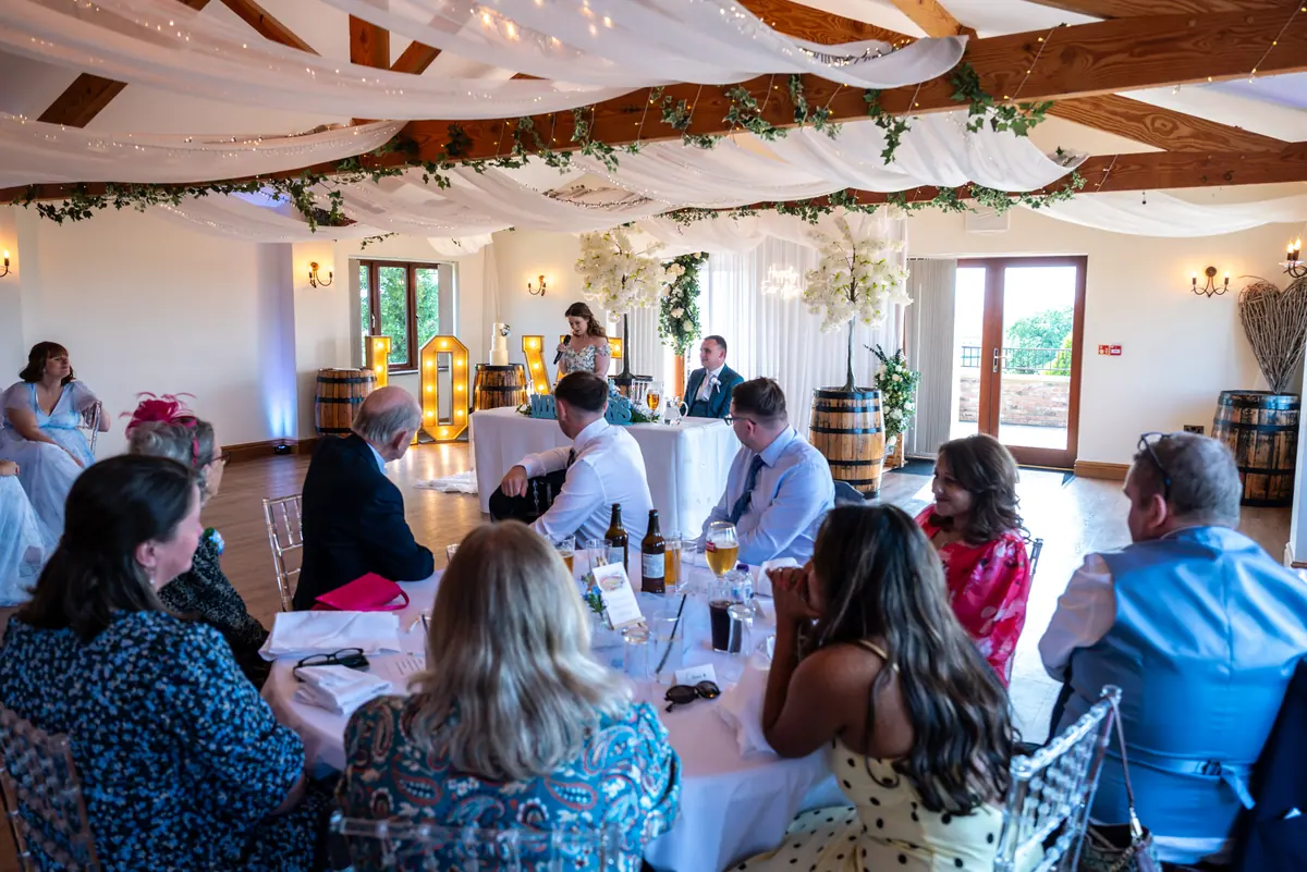 Guests seated at round tables beneath white drapes and hanging flowers