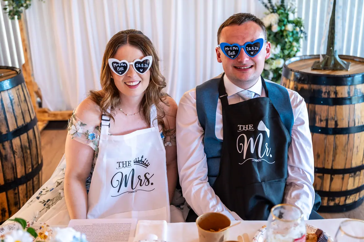 Megan and Dan wearing novelty sunglasses beside wooden barrels indoors