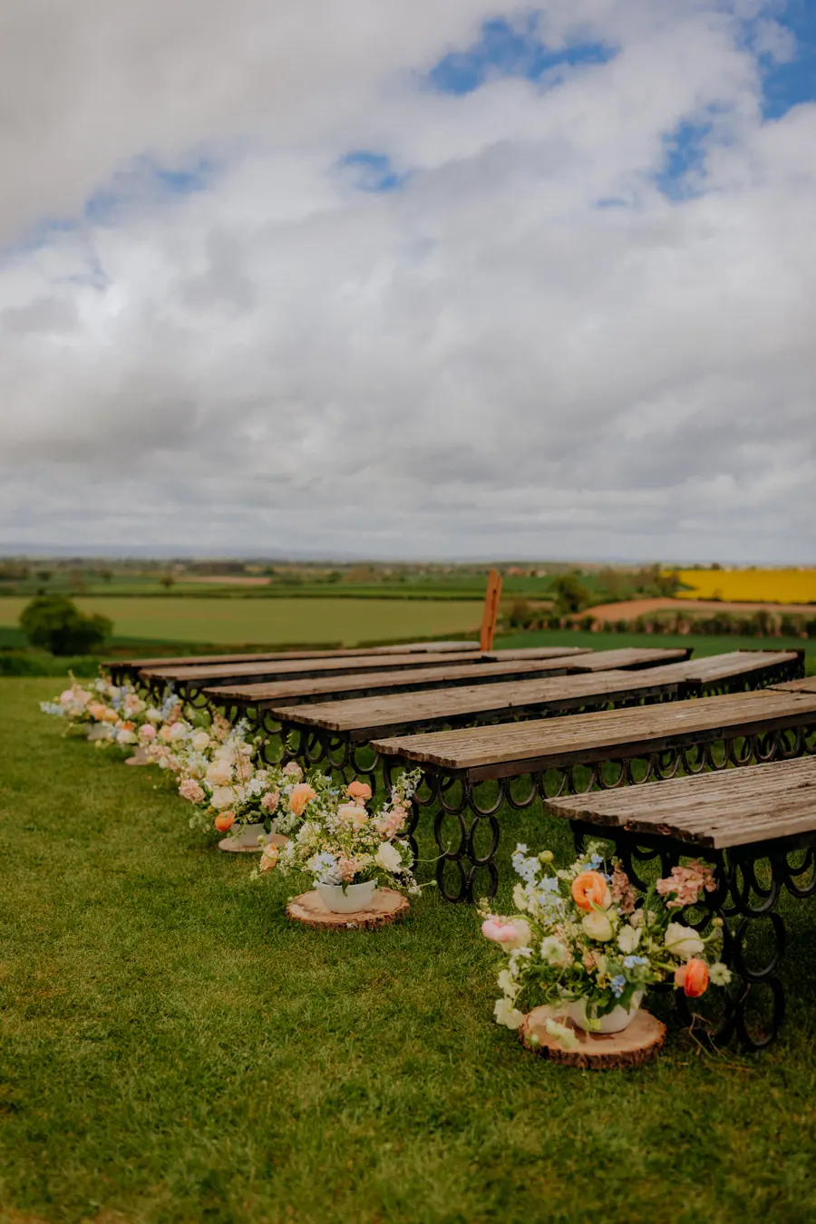 Outdoor ceremony benches lined with peach and white flowers beside the aisle