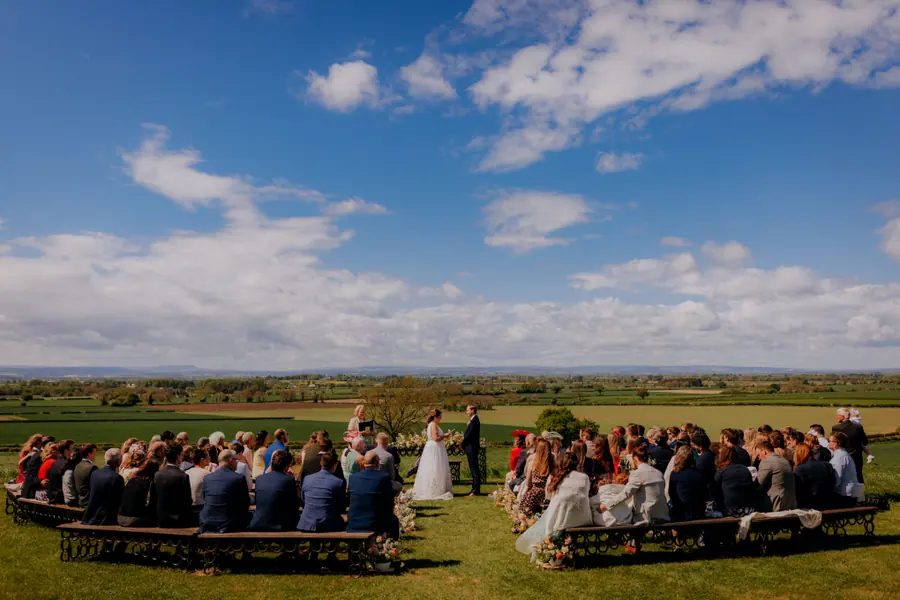Guests seated on horseshoe benches facing the couple and open fields