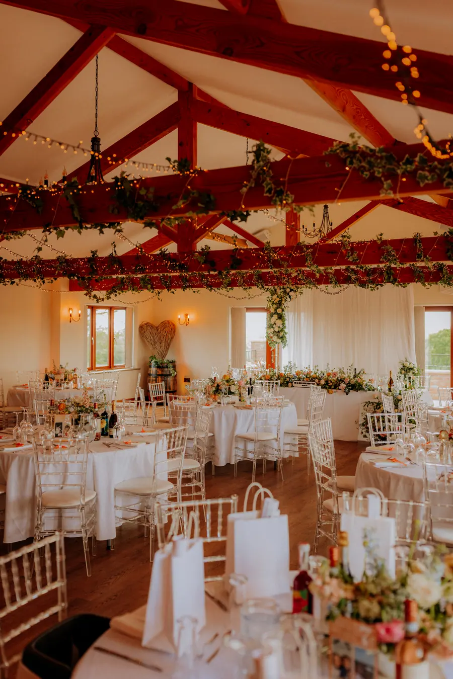 Peach and pink flowers across round tables beneath the wooden beams