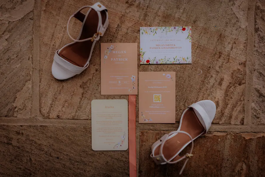 White shoes and peach stationery arranged across the wooden floor