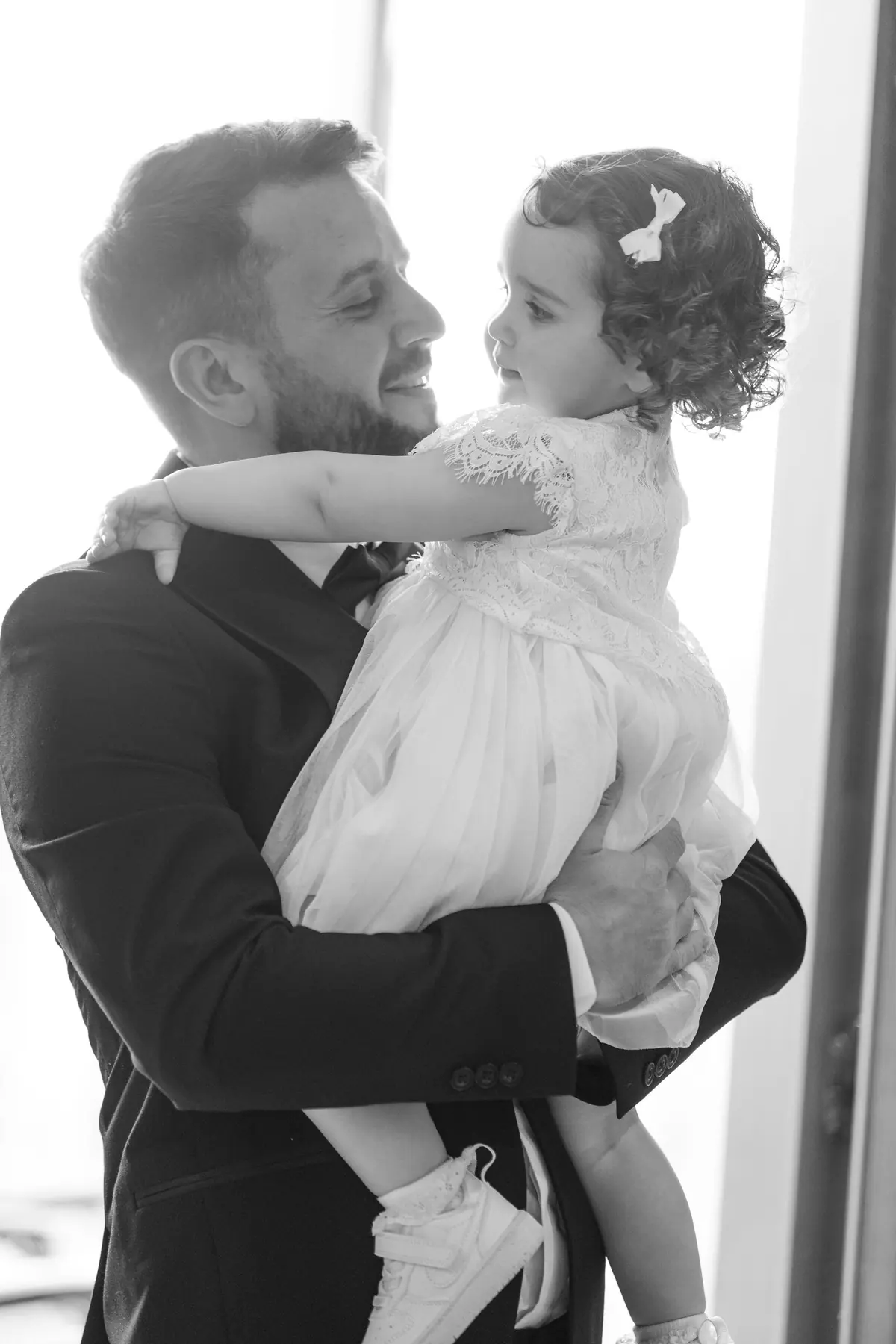 Alex holding a young girl in a pale dress near a window