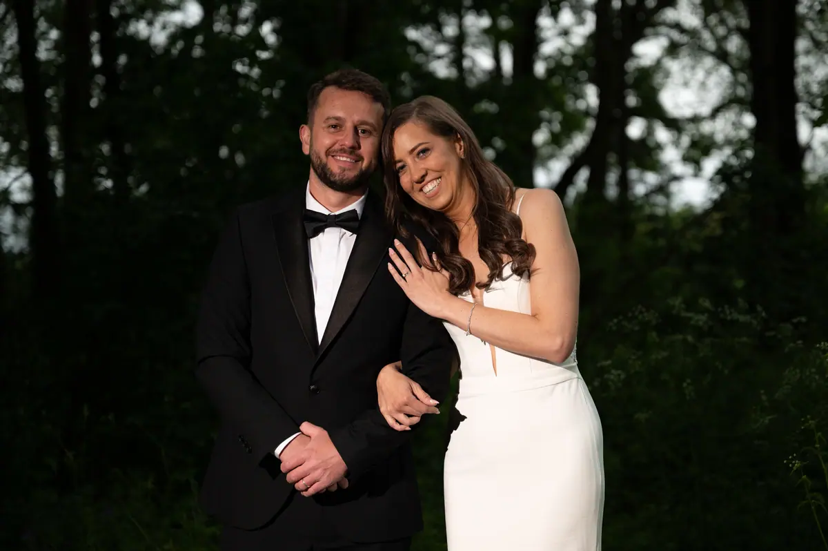 Natalie and Alex standing together beneath dark trees after sunset