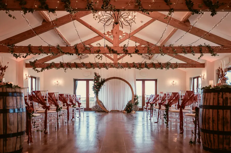 Indoor ceremony chairs facing a circular arch beneath dressed wooden beams