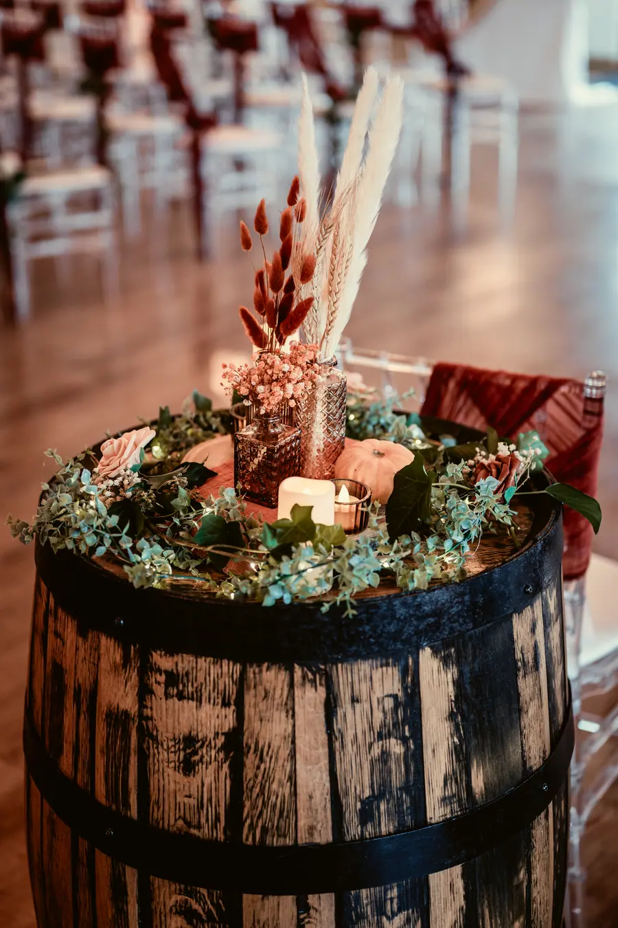 Autumn flowers, dried leaves and candles arranged on a dark wooden barrel