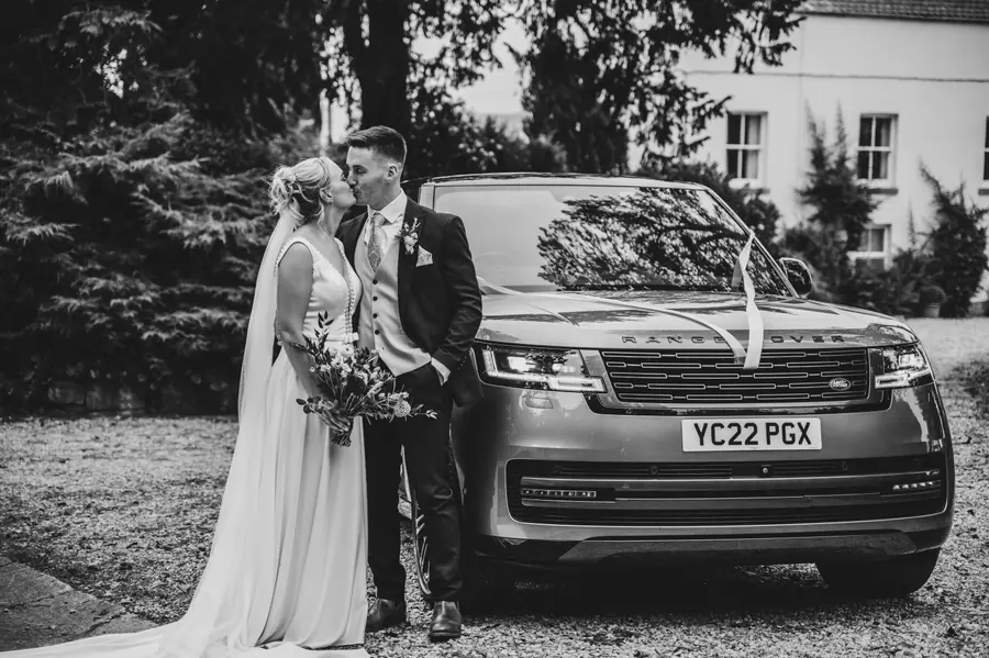 Olivia and Granville beside a dark car outside the venue in black and white