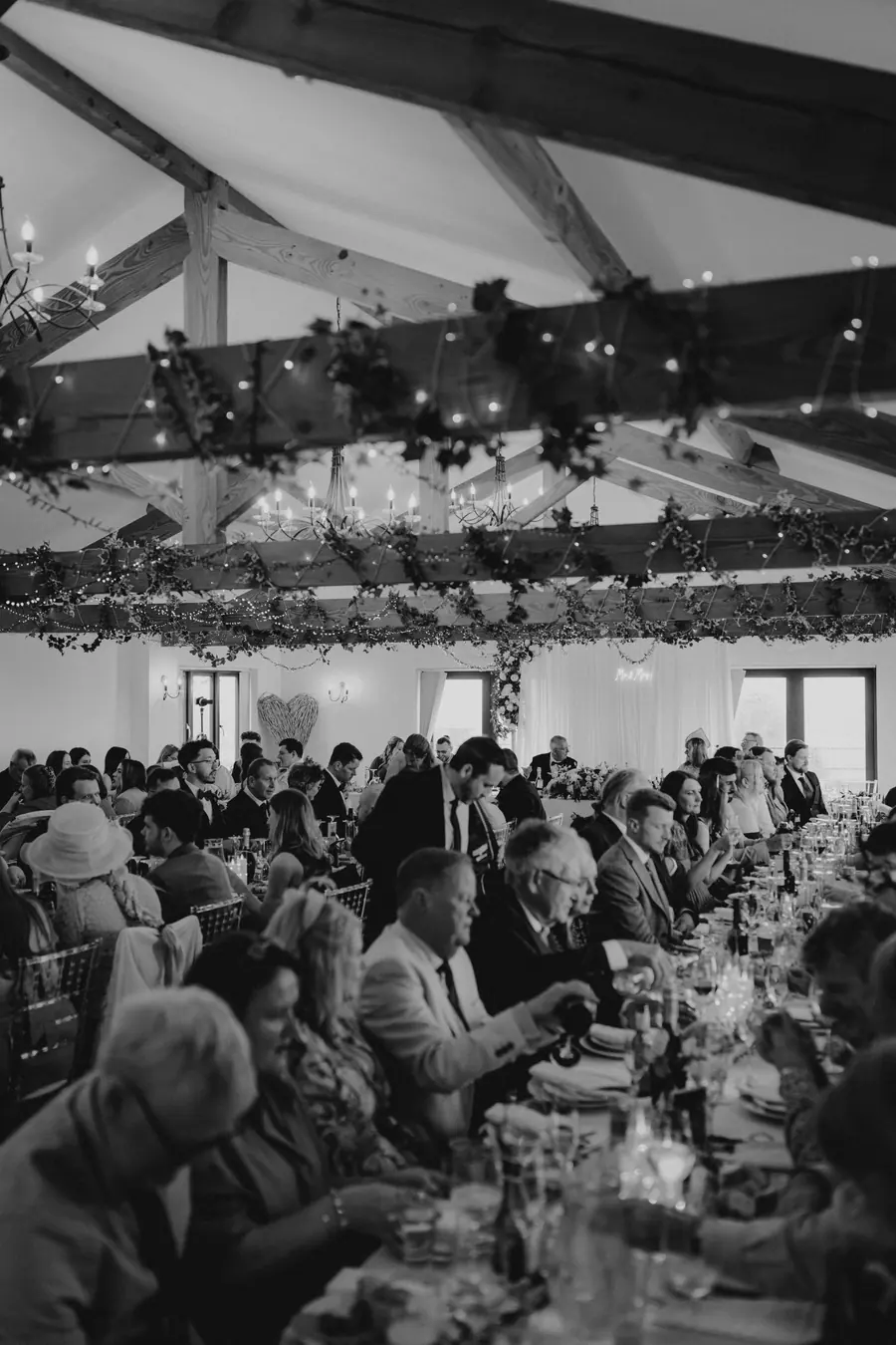 Guests seated along a long table beneath draped beams in black and white