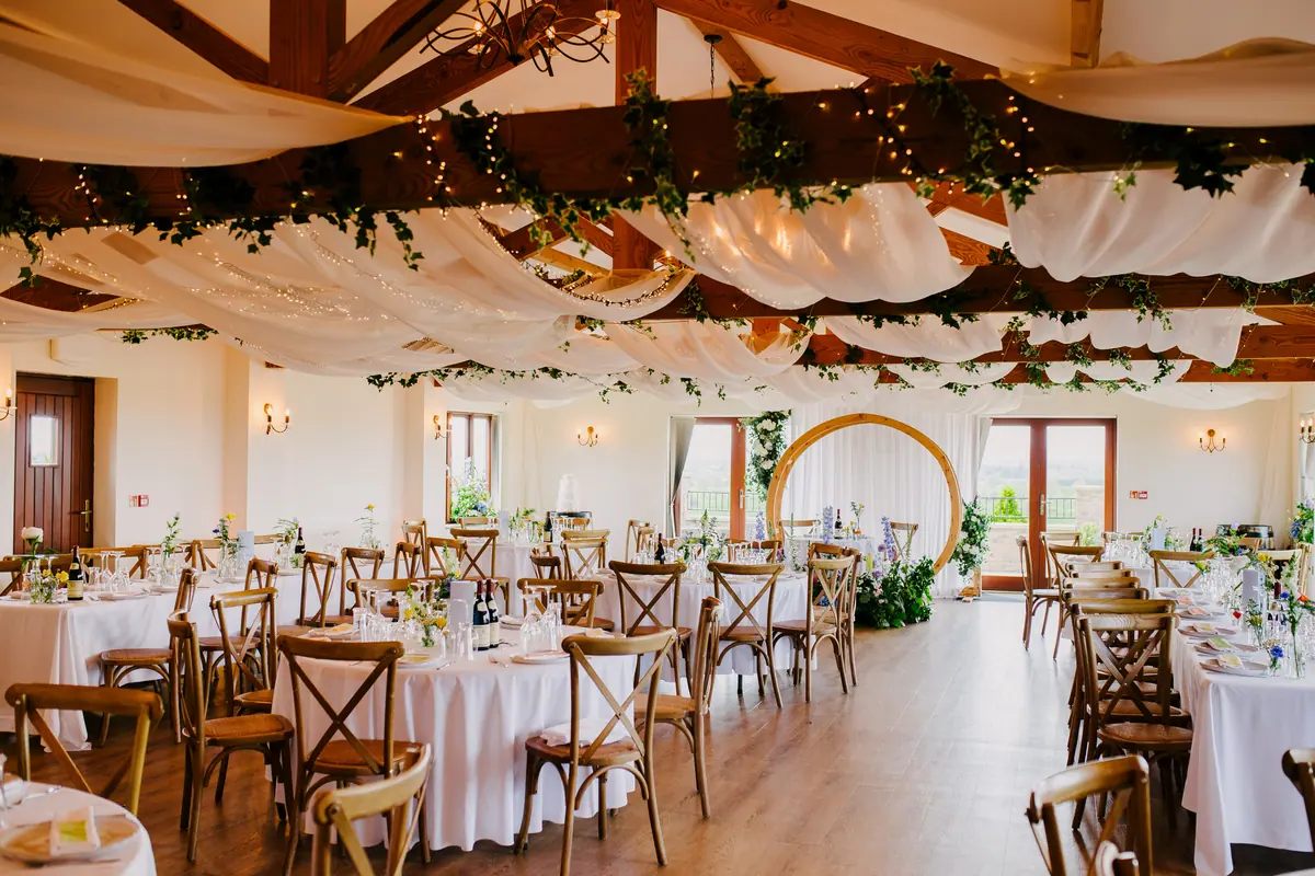 Round Hall tables and wooden chairs beneath white drapes and greenery