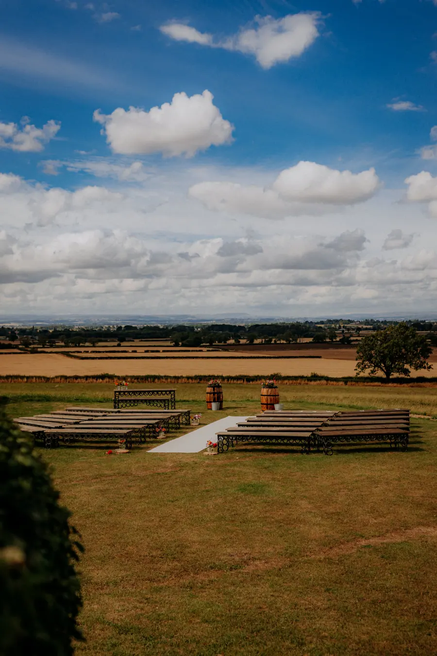 Outdoor ceremony benches looking across open fields beneath scattered clouds
