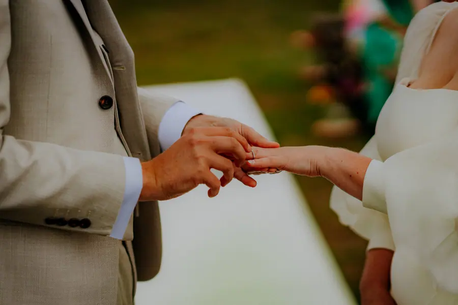 Ben placing a ring on Rae's hand during the outdoor ceremony
