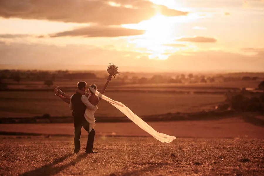 The couple embracing among hay bales beneath the low evening sun