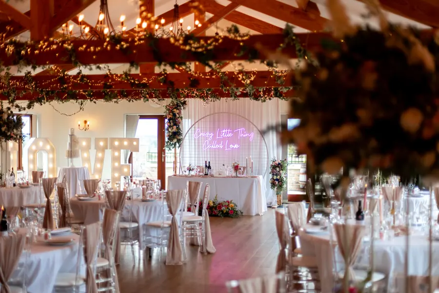 Round Hall tables beneath greenery and a pink neon sign