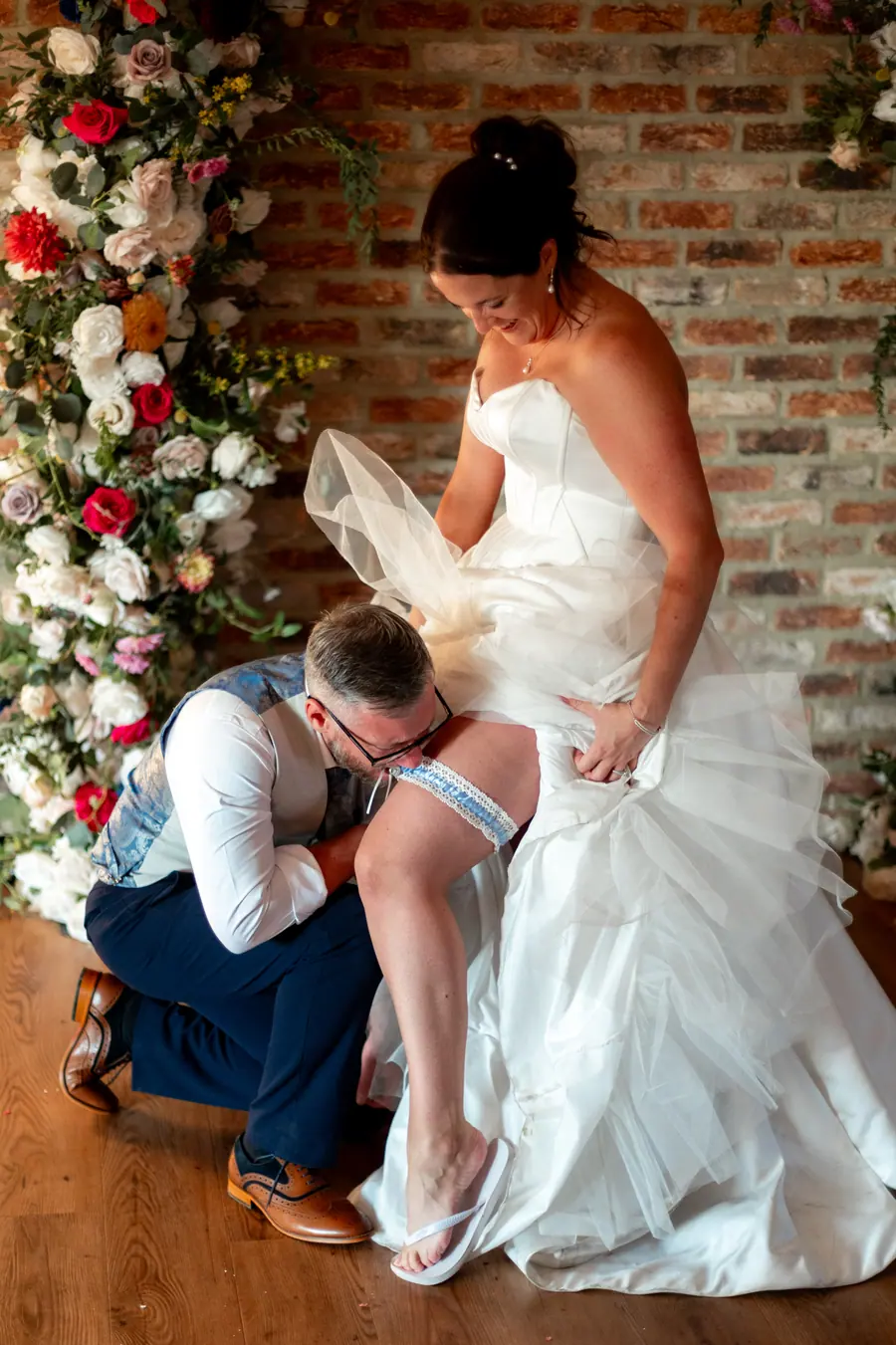 Luke fastening Stacey's shoe beside a red and white floral column