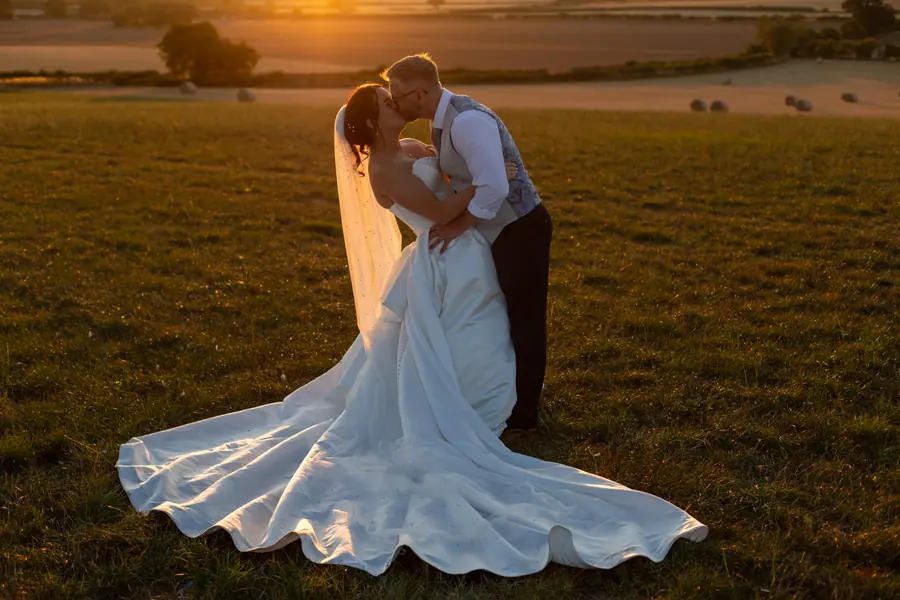 The couple kissing in the field beneath the low evening sun
