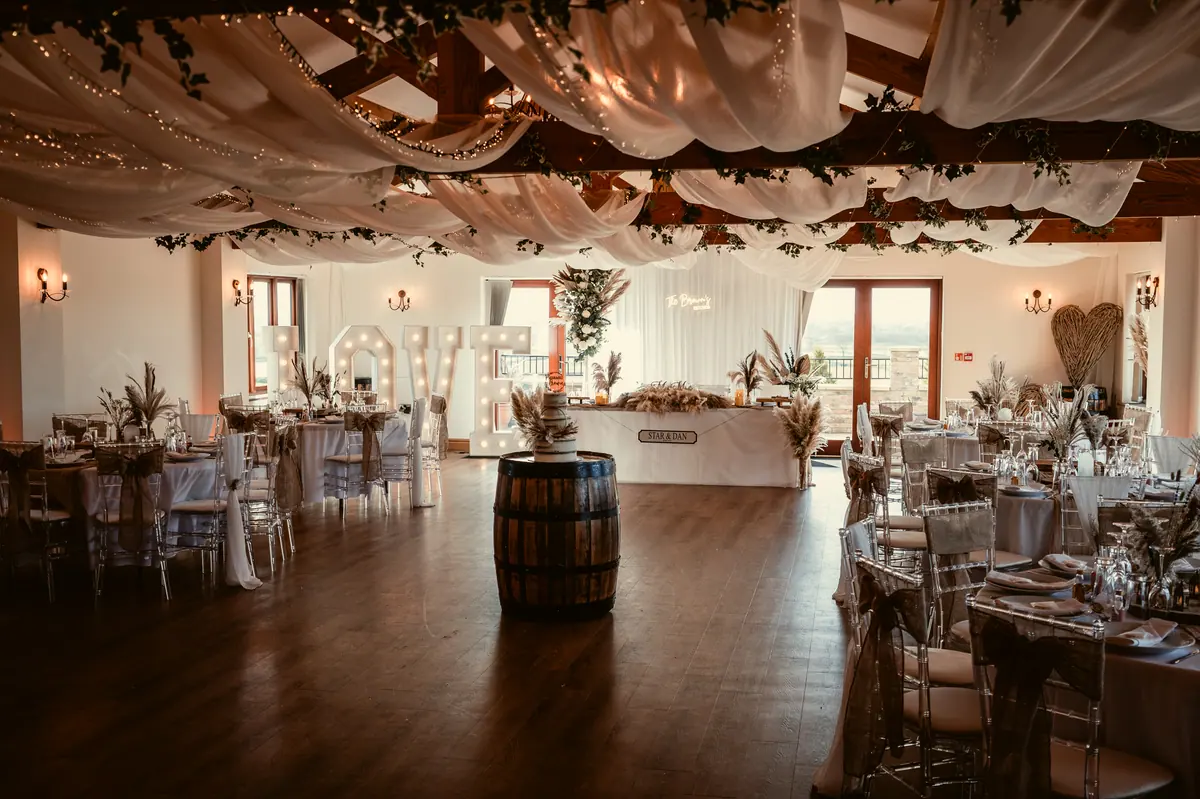 Round Hall tables arranged beneath white drapes, greenery and warm lights