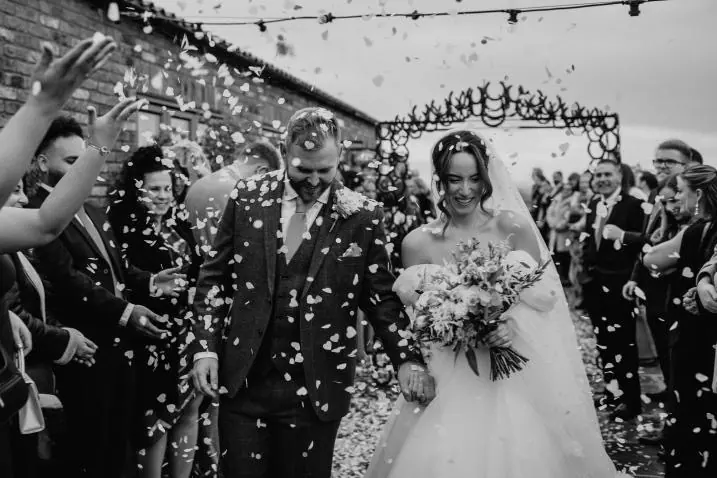Guests throwing confetti as the couple pass beneath the horseshoe arch