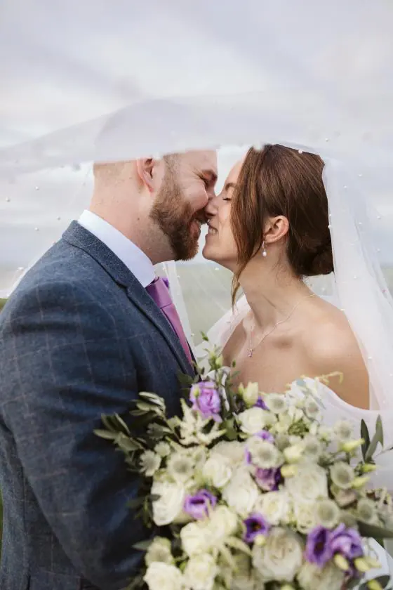 Zoe and Scott beneath her veil with white and purple flowers